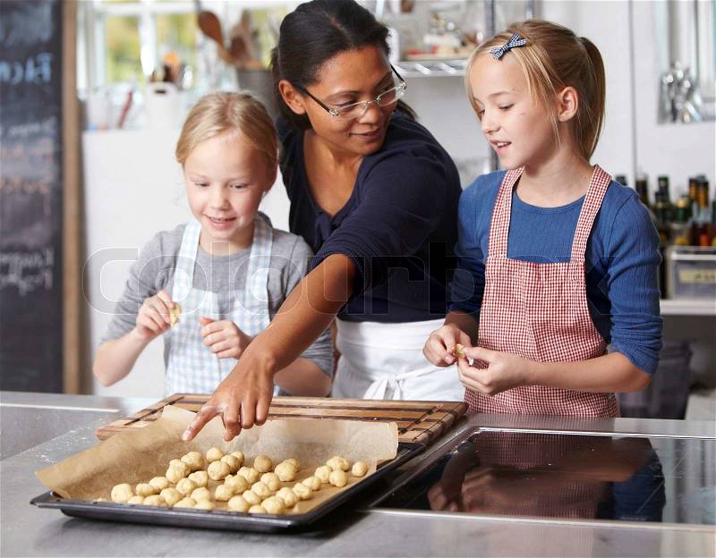 An asian woman teaching two caucasian girls how to bake cookies, stock photo