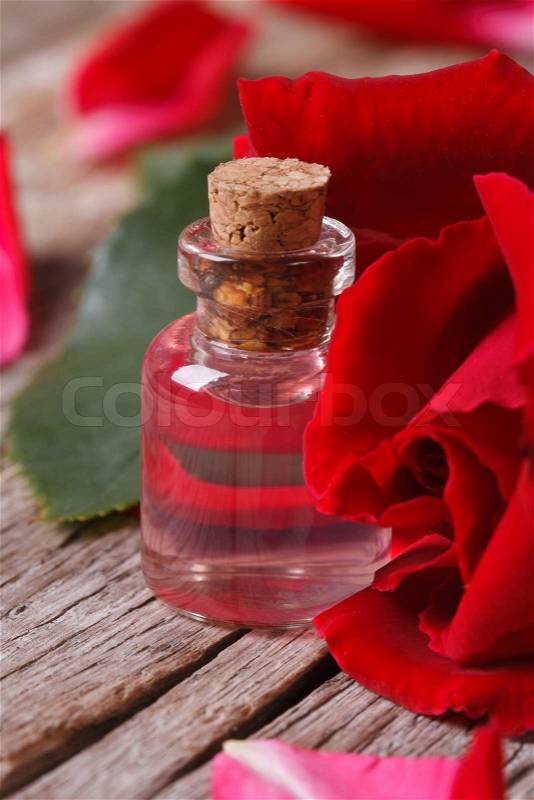 Rose water in a glass bottle on a background of red roses closeup vertical , stock photo