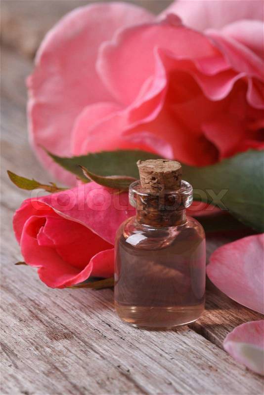 Rose water in a glass bottle on a background of pink roses close up vertical , stock photo