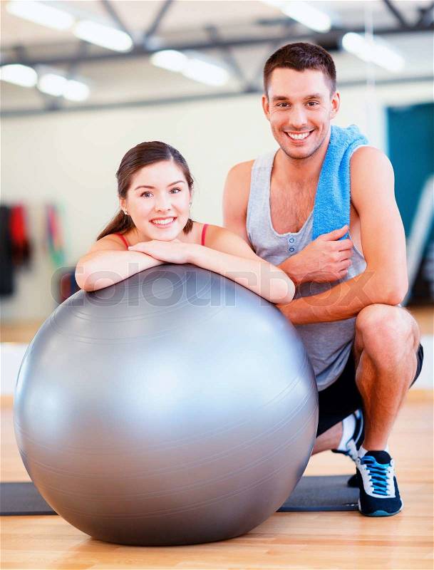 Fitness, sport, training, gym and lifestyle concept - two smiling people with fitness ball in the gym, stock photo