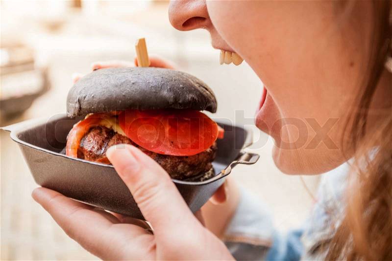 Portrait of woman biting black burger with marbled beef, stock photo