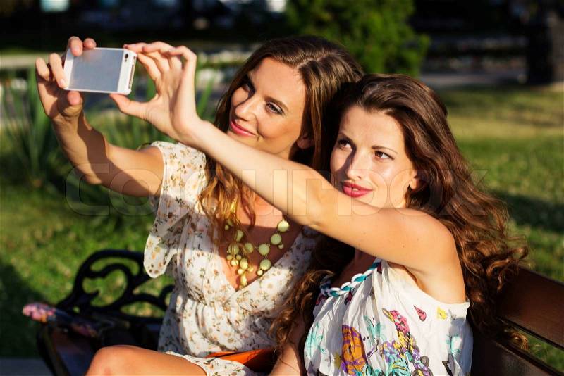 Outdoor portrait of two friends taking photos with a smartphone, stock photo
