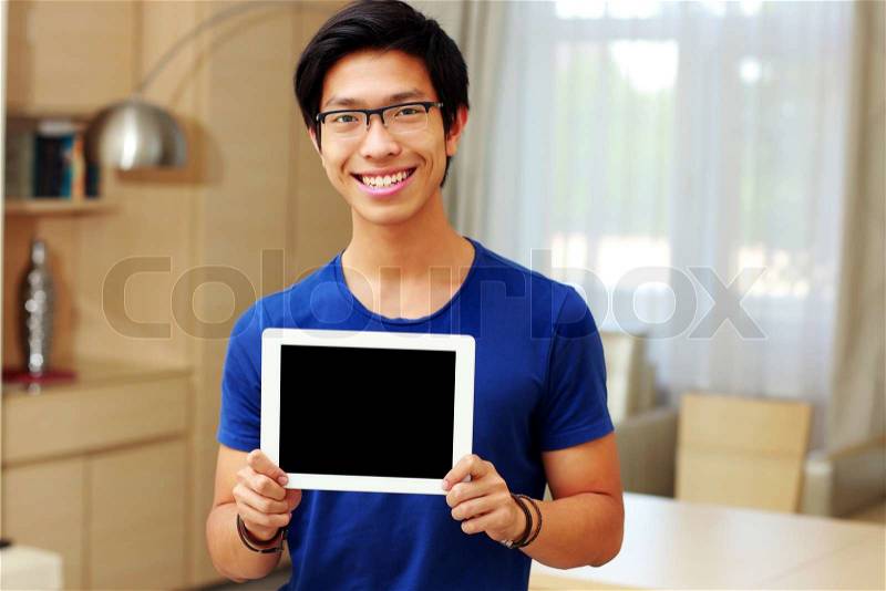 Young happy asian man showing tablet computer screen at home, stock photo
