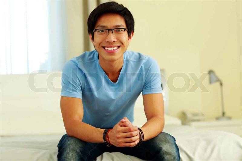 Happy asian man sitting on the bed at home, stock photo