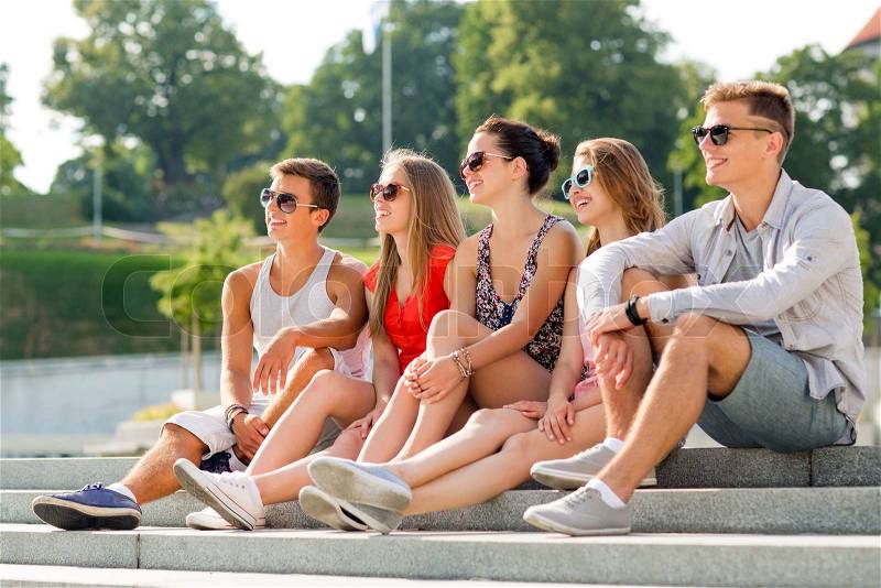 Friendship, leisure, summer and people concept - group of smiling friends sitting on city square, stock photo