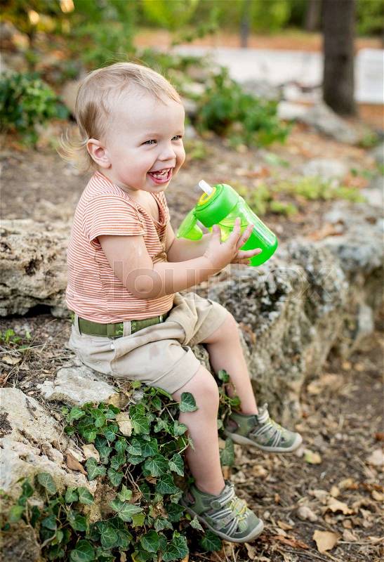 Happy toddler boy drinks water sitting, stock photo