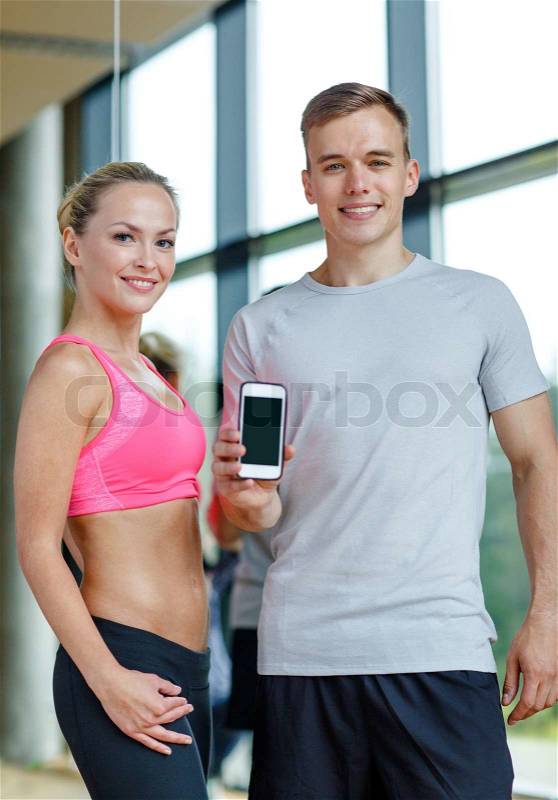 Fitness, sport, advertising, technology and diet concept - smiling young woman and personal trainer with smartphone blank screen in gym, stock photo