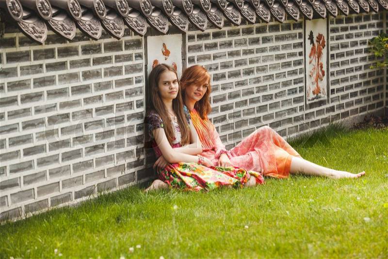 Two beautiful girls sitting at ancient korean park against brick wall, stock photo