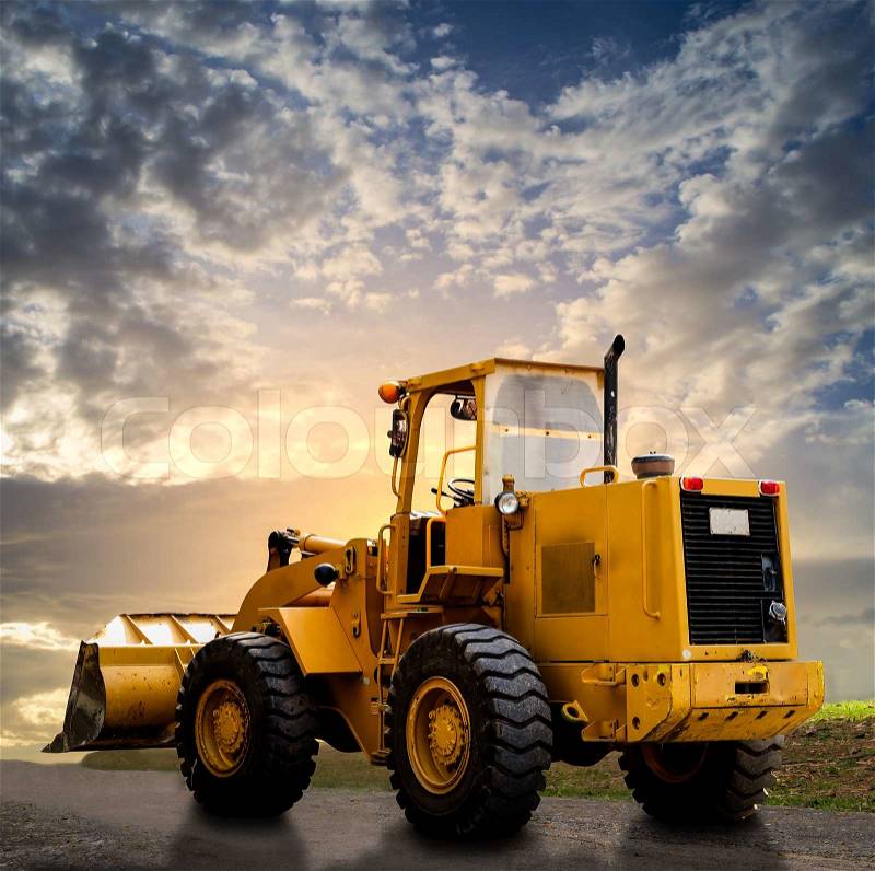 Yellow tractor on the road with cloudy blue sky, stock photo