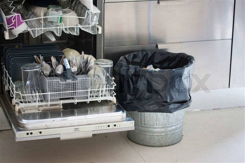 Dishwasher with dirty kitchen wares and a thrash bin, stock photo