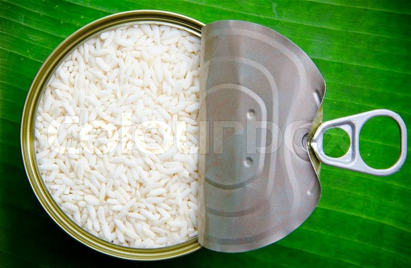 Raw sticky rice in can on leaves background, stock photo