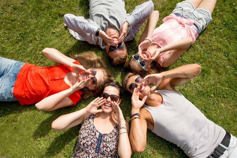 Friendship, leisure, summer and people concept - group of smiling friends lying on grass in circle outdoors, stock photo