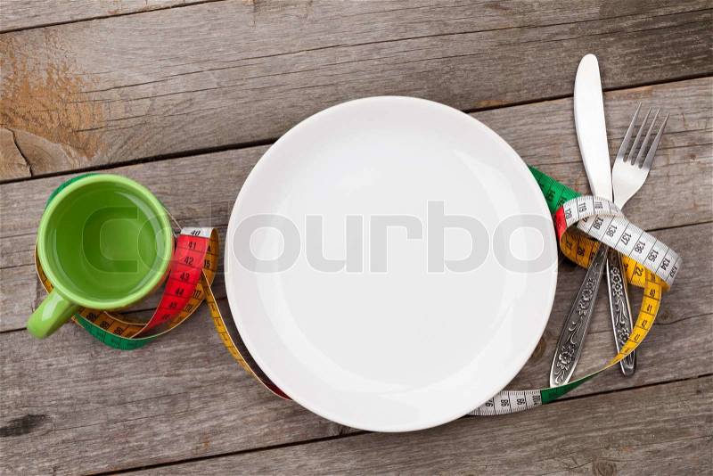 Plate with measure tape, cup, knife and fork. Diet food on wooden table, stock photo