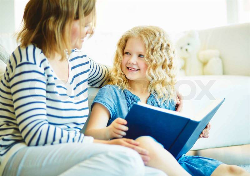 Portrait of cute girl listening to her mother telling an interesting story at home, stock photo
