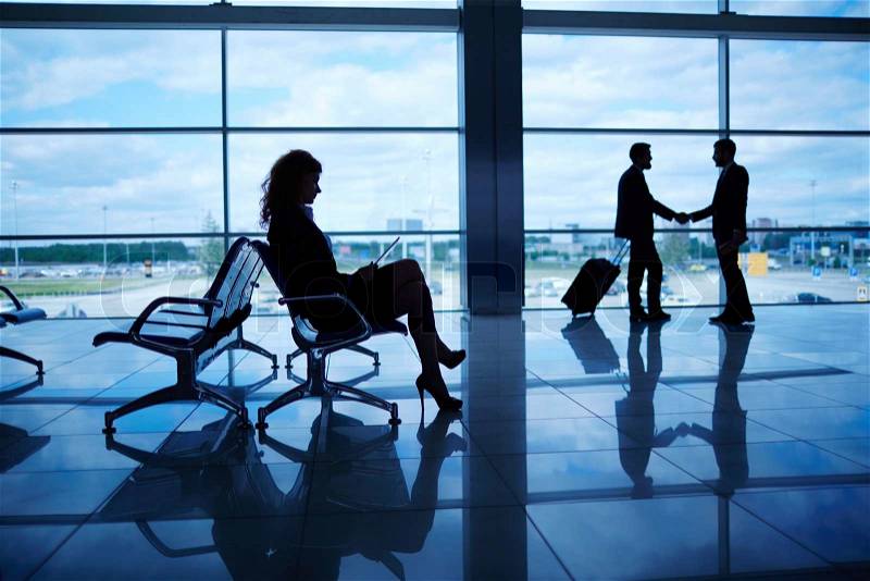 Outline of businesswoman sitting in airport on background of her colleagues handshaking by the window, stock photo