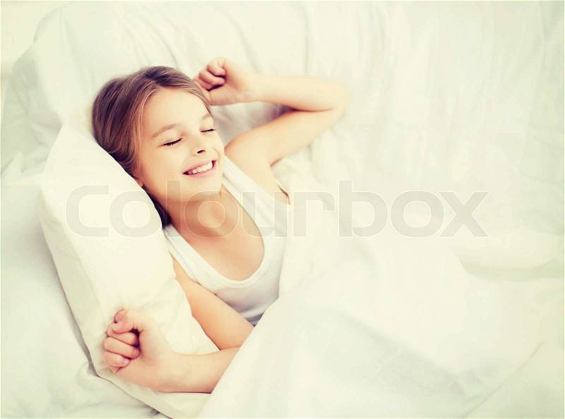 Health, beauty and childhood concept - smiling girl child waking up in bed at home, stock photo