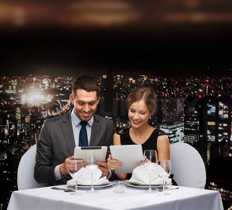 Restaurant, couple, technology and holiday concept - smiling couple with menus on tablet pc computers at restaurant, stock photo