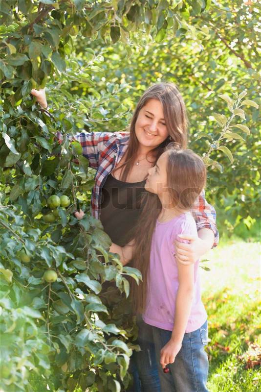 Happy smiling mother and daughter posing at apple garden at sunny day, stock photo
