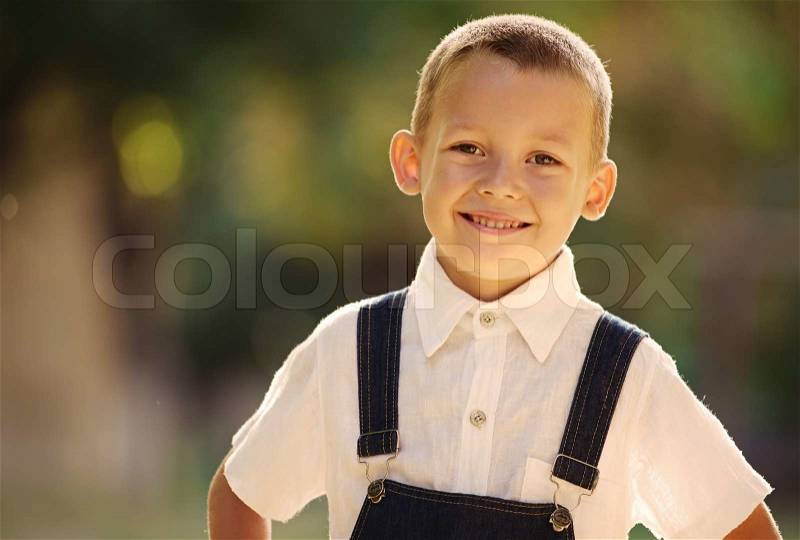 Smiling happy confident little boy posing outdoors in the summer sunshine looking at the camera with a beaming friendly smile, stock photo