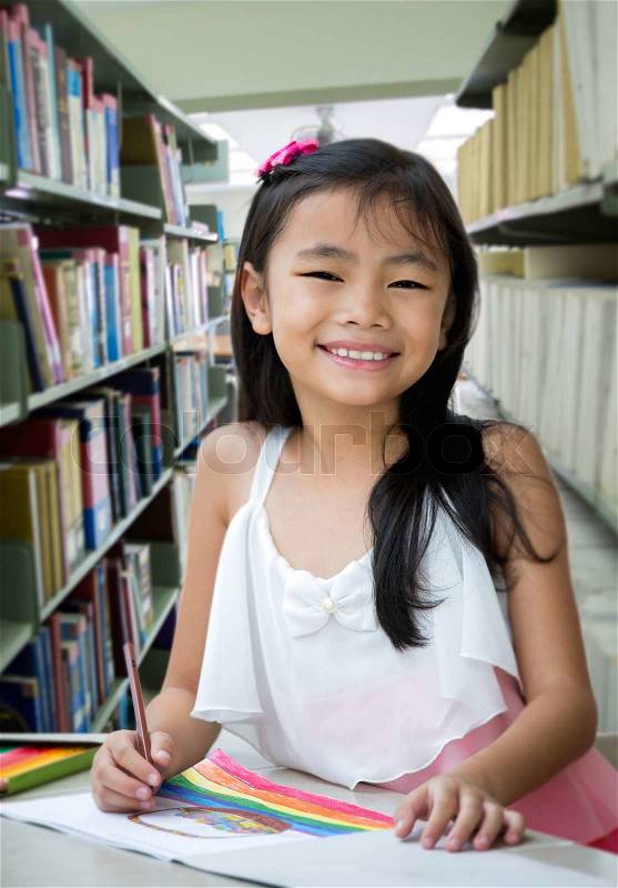Portrait of cute schoolgirl smiling while drawing a picture in library, stock photo