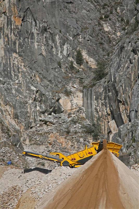 Machine crushing small pieces of marble to road materials in the mountains near the Italian city Carrara, stock photo