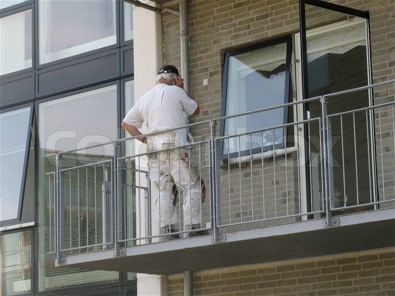 Painter talking in mobile phone on balcony in a new build apartment building, stock photo