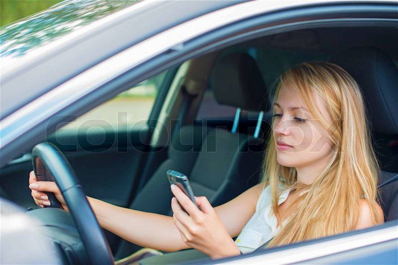 Beautiful young woman writing sms while driving car, stock photo
