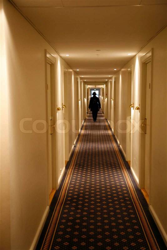 Black dressed person walking down a long hotel corridor. Motion blur, stock photo