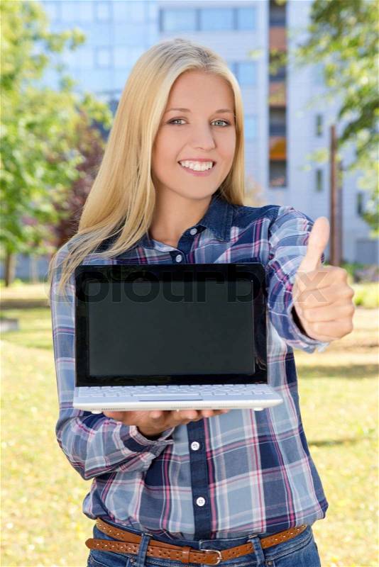 Beautiful smiling woman with laptop thumbs up in park, stock photo