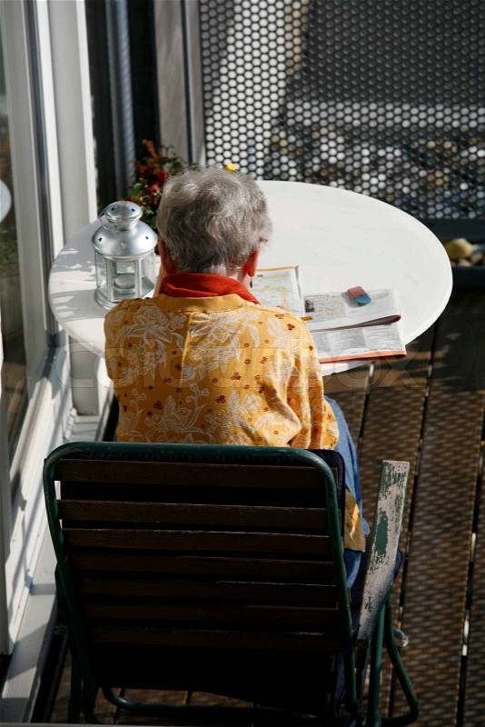 Retired female doing crossword puzzle at her balcony in the first spring sun, stock photo