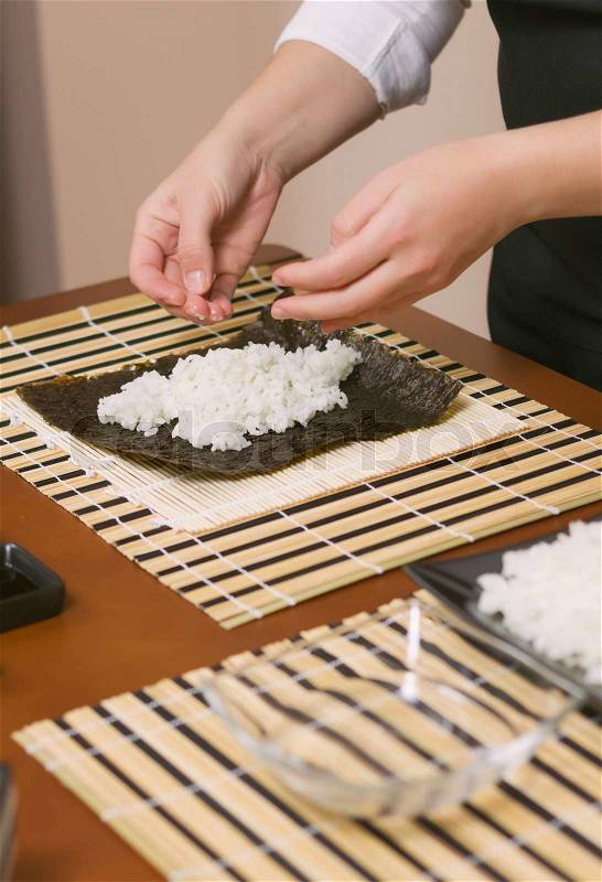 Hands of woman chef filling japanese sushi rolls with rice on a nori seaweed sheet, stock photo