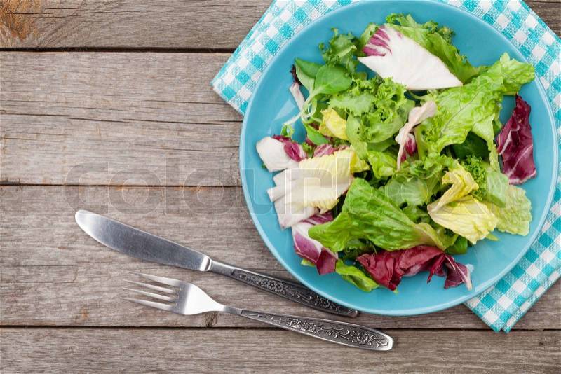 Plate with fresh salad, knife and fork. Diet food on wooden table with copy space, stock photo