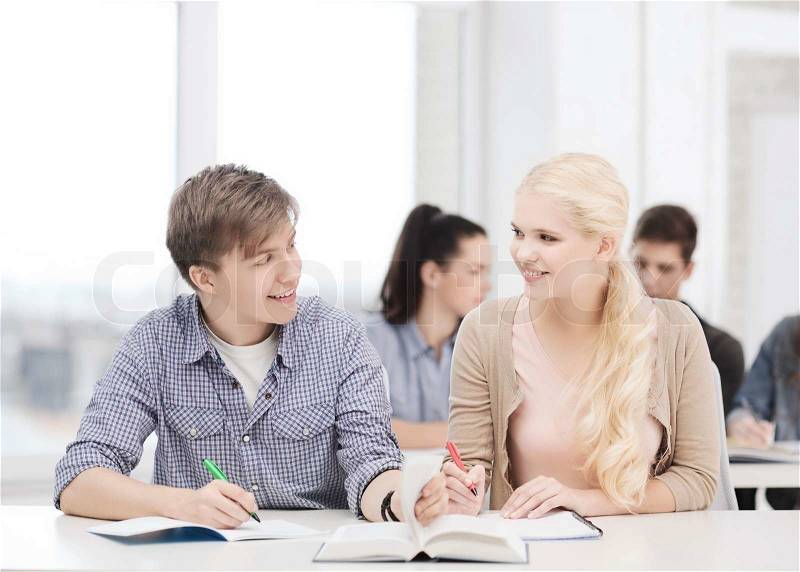 Education, school and people concept - two teenagers with notebooks and book looking at each other at school, stock photo