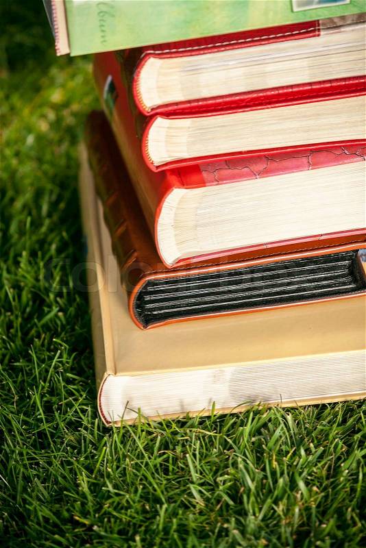 Closeup photo of pile of colored books lying on grass at sunny day, stock photo