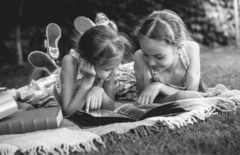 Black and white photo of young girls looking at family photo album, stock photo
