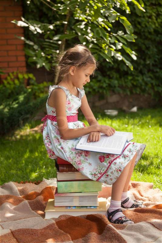 Cute smart girl reading big book at park at sunny day, stock photo