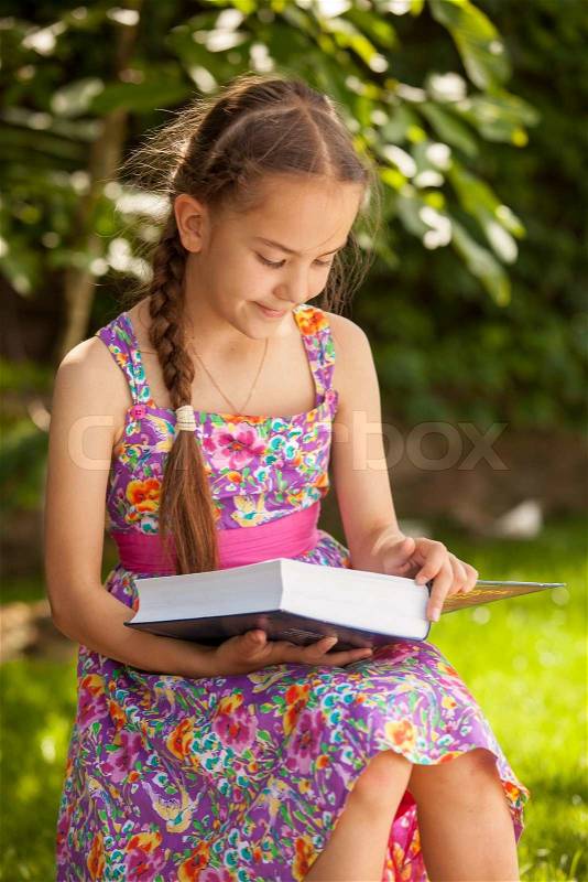 Portrait of cute brunette girl reading big book at forest, stock photo