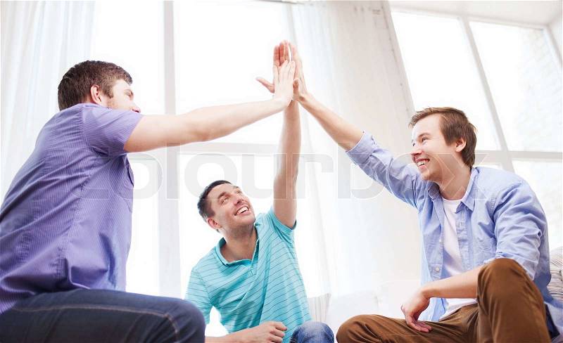 Teamwork, friendship and happiness concept - smiling male friends giving high five at home, stock photo