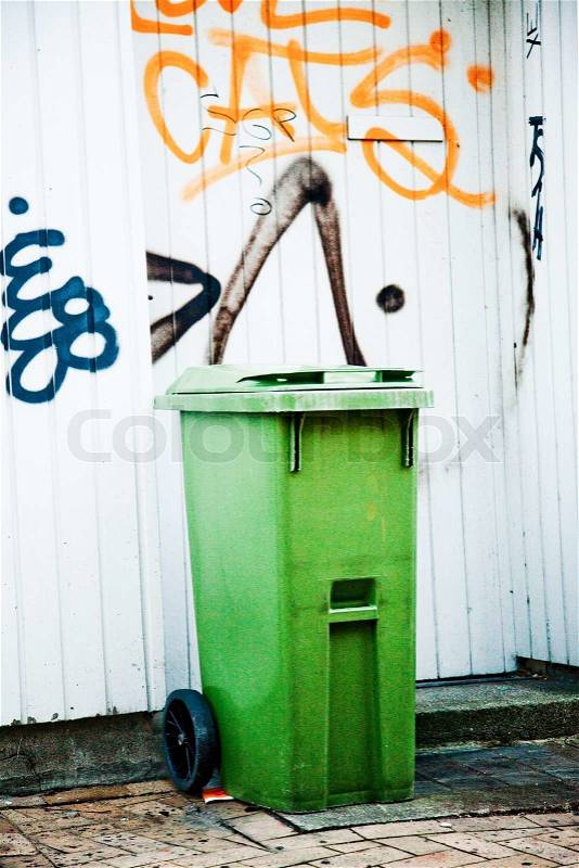 Green garbage bin in front of a graffiti wall, stock photo