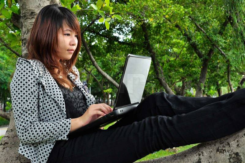 Portrait of beautiful woman sitting on the tree and playing laptop, stock photo