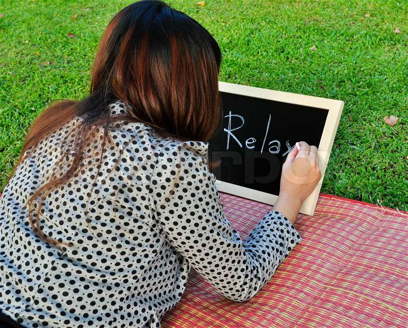 Woman lie down on the grass and write relax word on the blackboard, stock photo