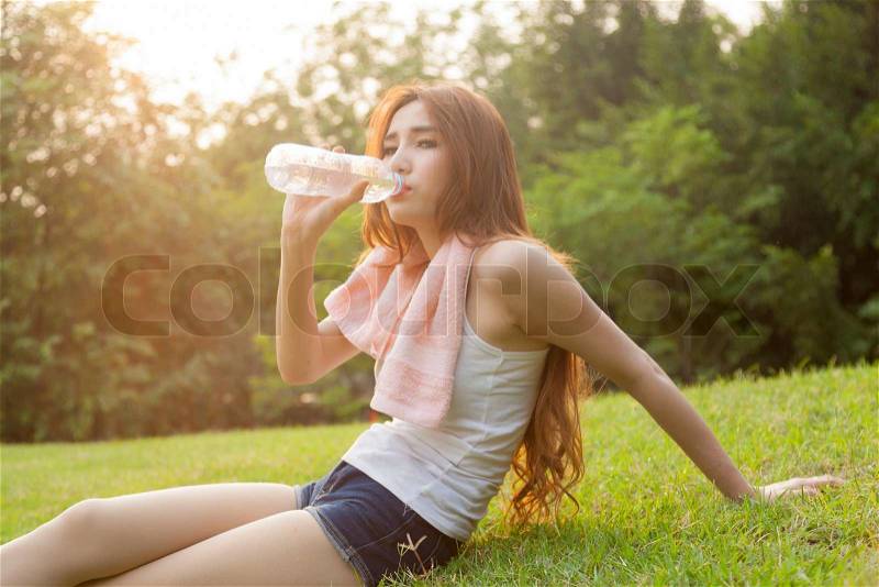 Woman sit and drink after exercise. On the lawn after a workout in the park, stock photo
