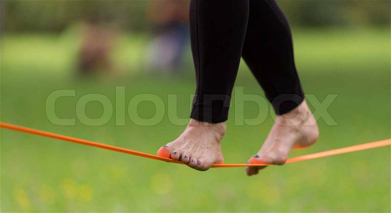 Lady practising slack line in the city park. Slacklining is a practice in balance that typically uses nylon or polyester webbing tensioned between two anchor points, stock photo