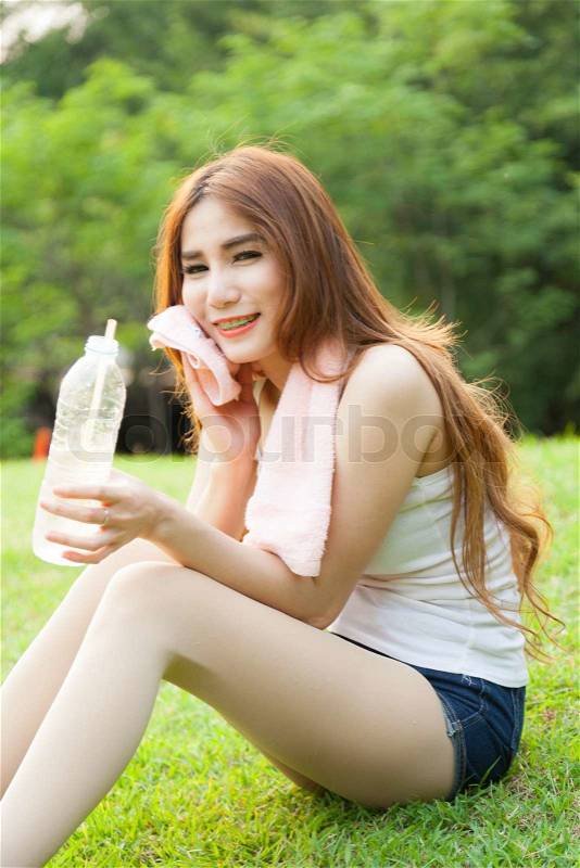 Woman sit and drink after exercise. On the lawn after a workout in the park, stock photo