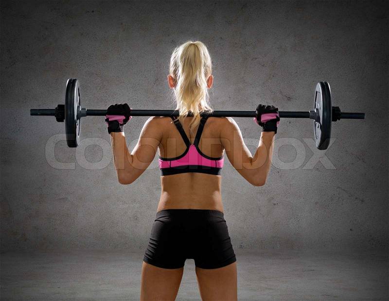 Fitness, sport and dieting concept - sporty woman exercising with barbell from back over concrete wall background, stock photo