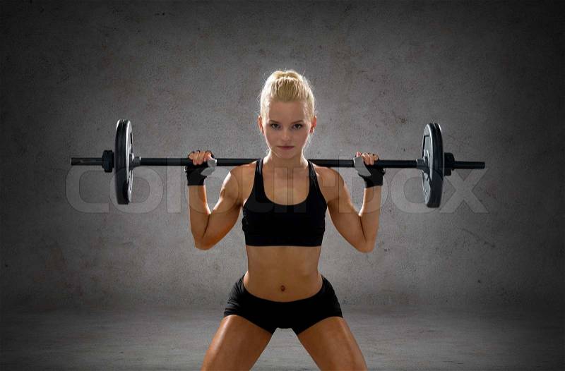 Fitness, sport and dieting concept - sporty woman exercising with barbell over concrete wall background, stock photo
