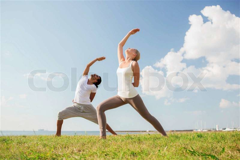 Fitness, sport, friendship and lifestyle concept - smiling couple making yoga exercises outdoors, stock photo