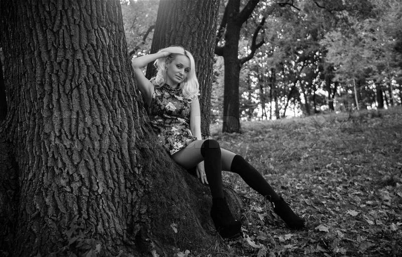 Outdoor monochrome shot of sexy woman sitting under big tree at forest, stock photo