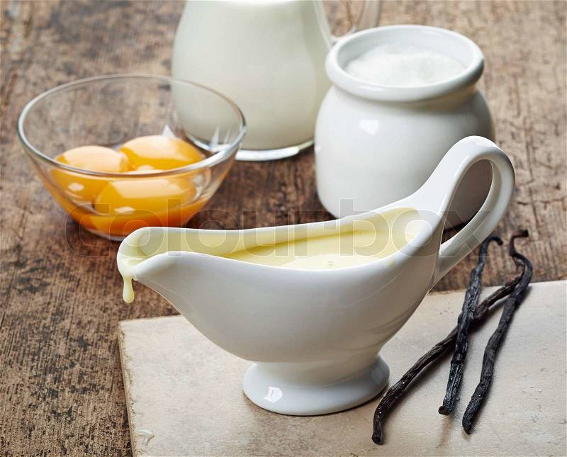 Sauceboat with vanilla sauce and ingredients on wooden table, stock photo