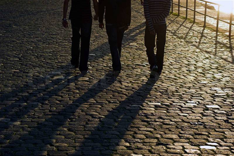 Young men walking in the sun on cobblestone road, stock photo